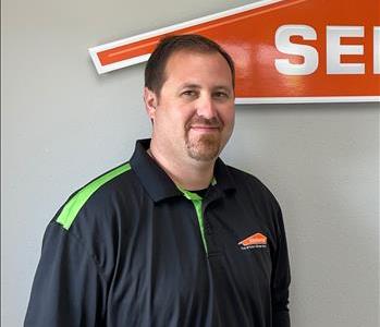 Male employee with dark hair smiling in front of SERVPRO sign
