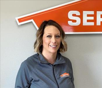 Woman employee with brown hair smiling standing in front of a SERVPRO sign