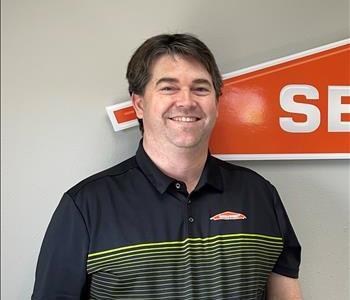 Male employee with dark hair smiling in front of a SERVPRO sign