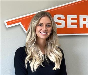 Female employee with blonde hair smiling in front of a SERVPRO sign