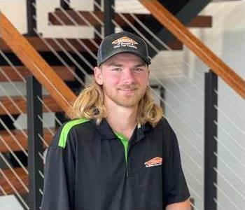 Male employee with light long hair smiling in front of SERVPRO sign