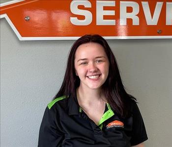 Female employee with dark hair smiling in front of a SERVPRO sign