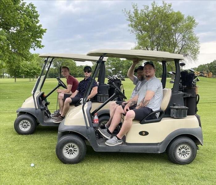 4 guys on golf carts at company golf outing