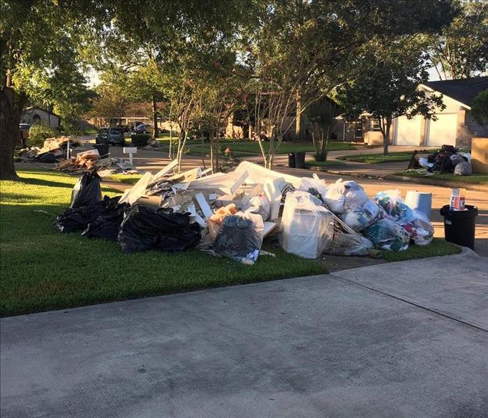 Debris bagged up in trash bags and sitting in a home owners green yard. 